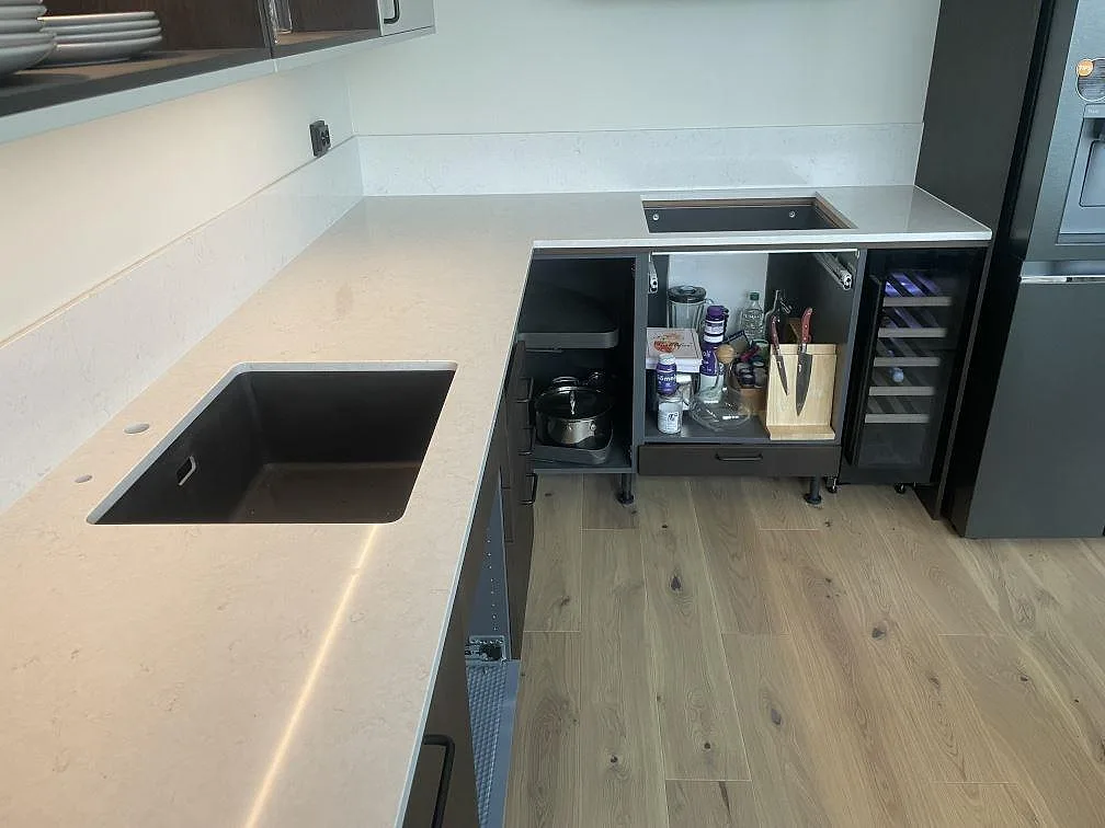 Mörk underlimmad diskho i ljus Silestone Snowy Ibiza vid ett hörn med vinkyl och mörka skåp i ett kök i Stockholm.
