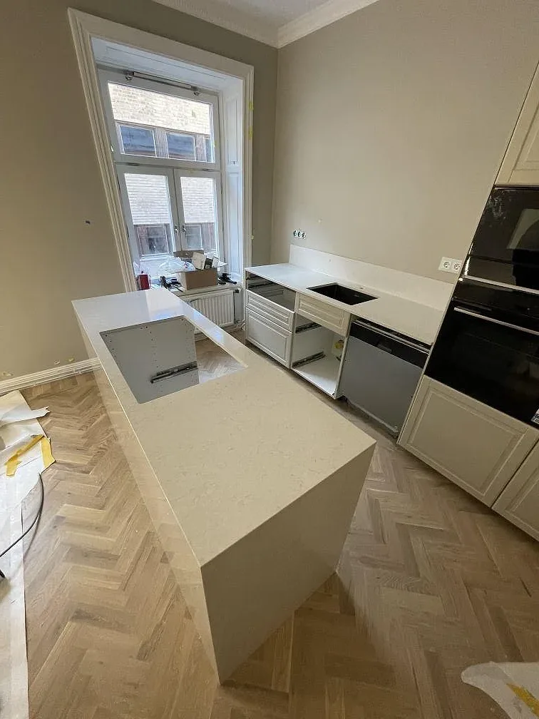 Köksbänkskiva i vit Silestone Snowy Ibiza vid fönster i ett Stockholmskök under montering, med vita stommar och fiskbensparkett.