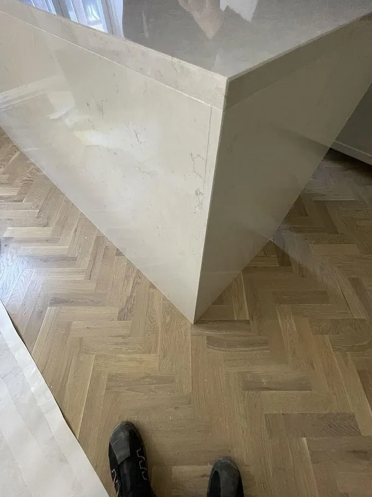 Köksö i vit polerad Silestone Snowy Ibiza med gerad waterfall-kant ned mot fiskbensparketten i ett kök i Stockholm.