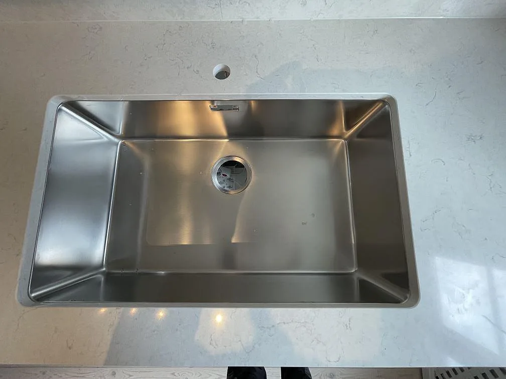 Underlimmad rostfri diskho med bred enkelho infälld i polerad vit Silestone Snowy Ibiza bänkskiva i ett kök i Stockholm.