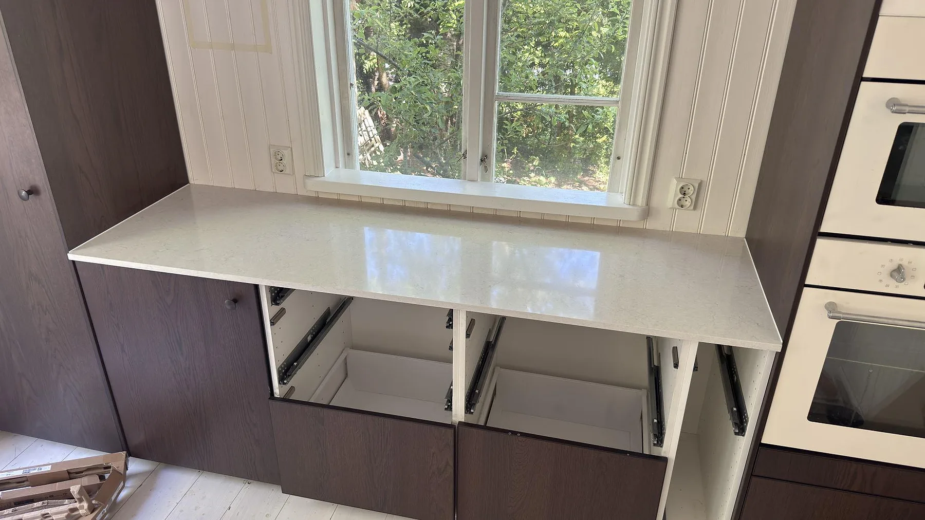 Kort köksbänksektion i vit Silestone Snowy Ibiza under ett fönster i ett Stockholmskök, polerad yta över mörka stommar med utdragna sopkärl.