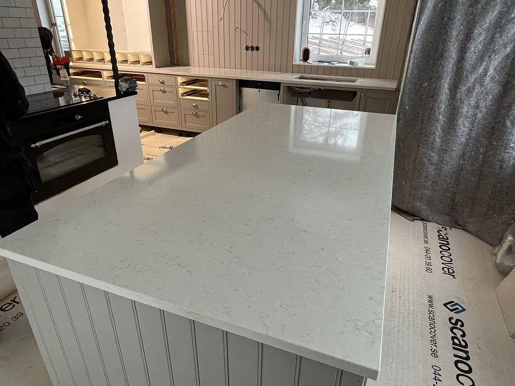 Polerad köksbänkskiva och köksö i vit Silestone Snowy Ibiza komposit med ljus ådring under montering i Stora Vika.