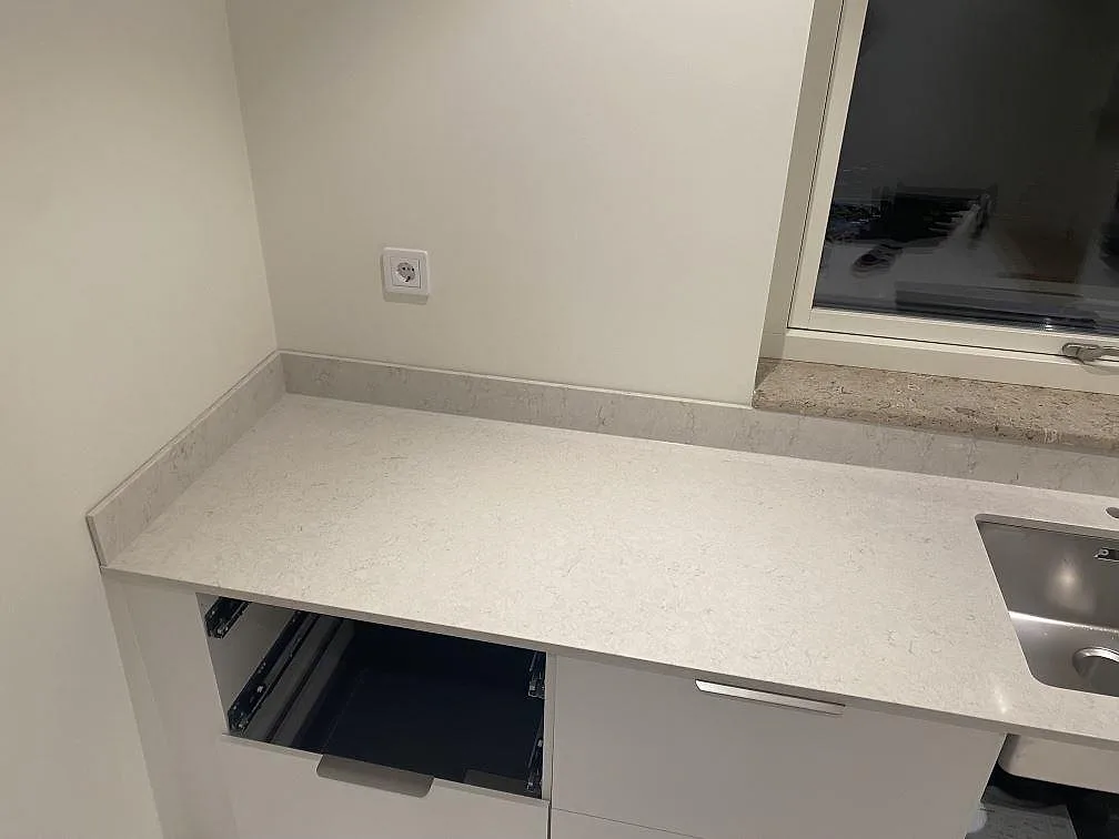 Vänster bänksträcka i Strandbaden med polerad Silestone Snowy Ibiza som köksbänkskiva, låg stänkkant och arbetsyta intill diskhon.