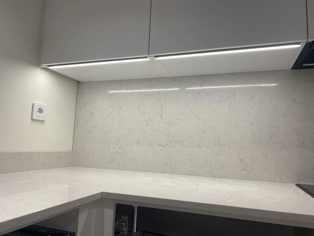 Polerad väggskiva och bänkskiva i Silestone Snowy Ibiza med grå ådring under överskåp i ett kök i Strandbaden.