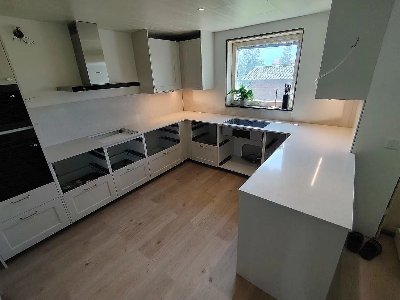 Polerad köksbänkskiva i vit Silestone Snowy Ibiza komposit med halvö, hällzon och matchande stänkskydd i ett kök i Sundborn.