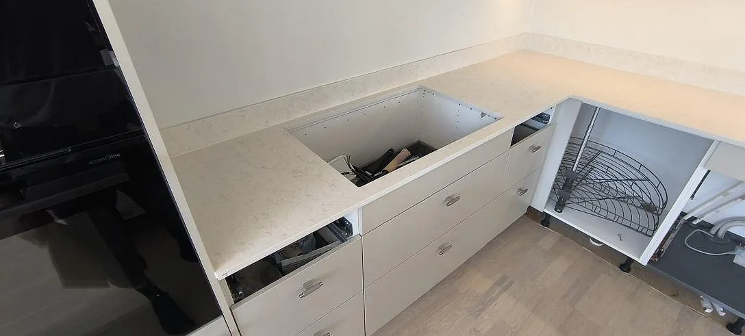 L-formad bänkskiva i matt Silestone Snowy Ibiza komposit med väggnära stänkkant under montering i Sundbyberg.