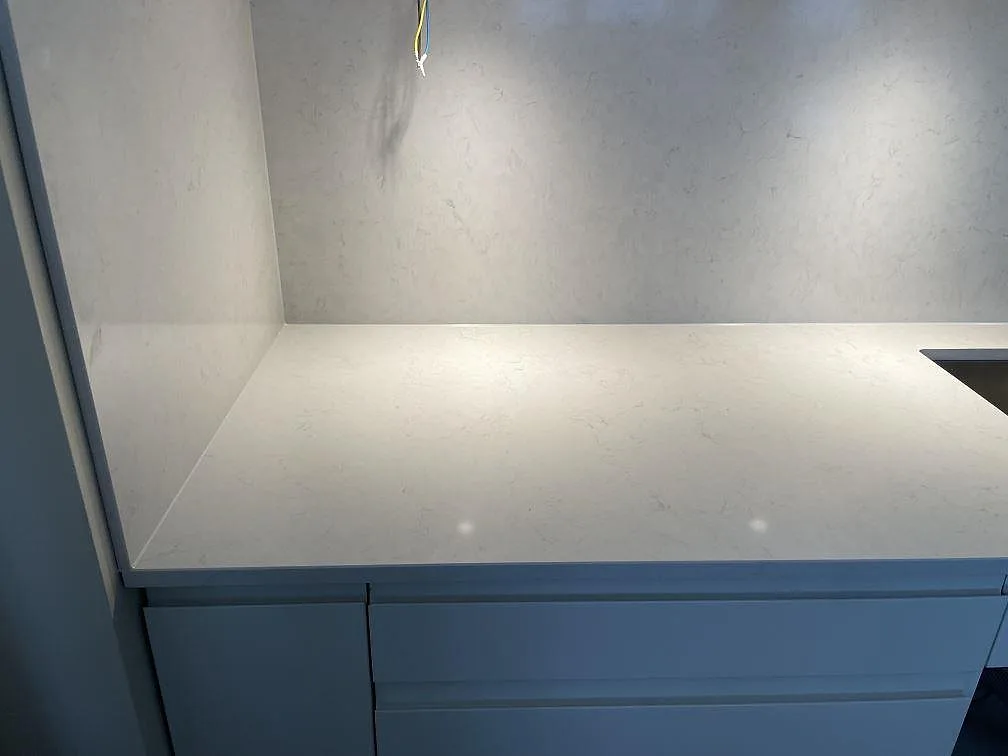 Hörn av köksbänkskivan i Silestone Snowy Ibiza med stänkskydd och kanten av en underlimmad rostfri diskho i ett kök i Sundbyberg.