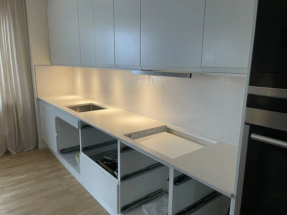 Lång köksbänk i polerad Silestone Snowy Ibiza med uppvikt stänkskydd, underlimmad rostfri diskho och tom hällurtagning, sedd från sidan i ett kök under montering i Sundbyberg.