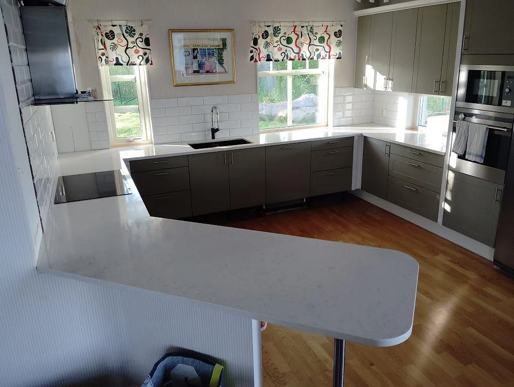 Köksbänkskiva i polerad Silestone Snowy Ibiza, 30 mm komposit, med halvö, häll och grå köksluckor i Svartsjö.