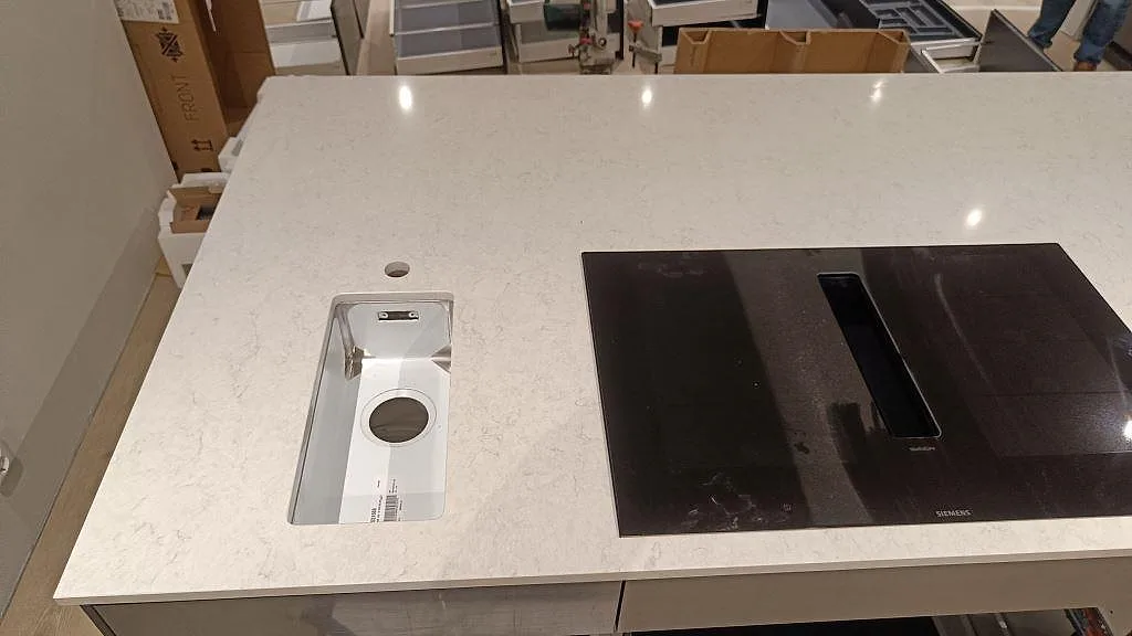 Närbild på köksö i polerad Silestone Snowy Ibiza med underlimmad diskho och Siemens induktionshäll i ett kök i Svedala.