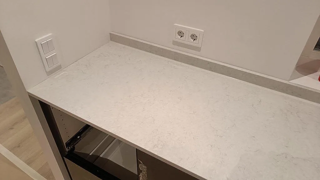 Bänkskiva i vit Silestone Snowy Ibiza med uppvikt stänkkant och eluttag längs väggen i ett kök i Svedala.