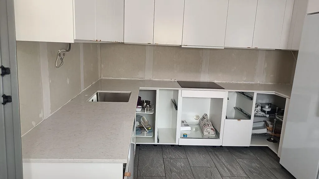 L-formad köksbänkskiva i polerad Silestone Snowy Ibiza, vit kvartskomposit med underlimmad rostfri diskho och svart häll i ett kök under montering i Svedala.