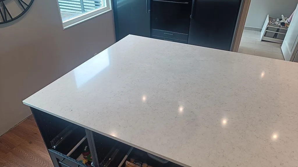 Polerad Silestone Snowy Ibiza på köksö med subtil grå ådring och mörka högskåp i kök i Svedala.