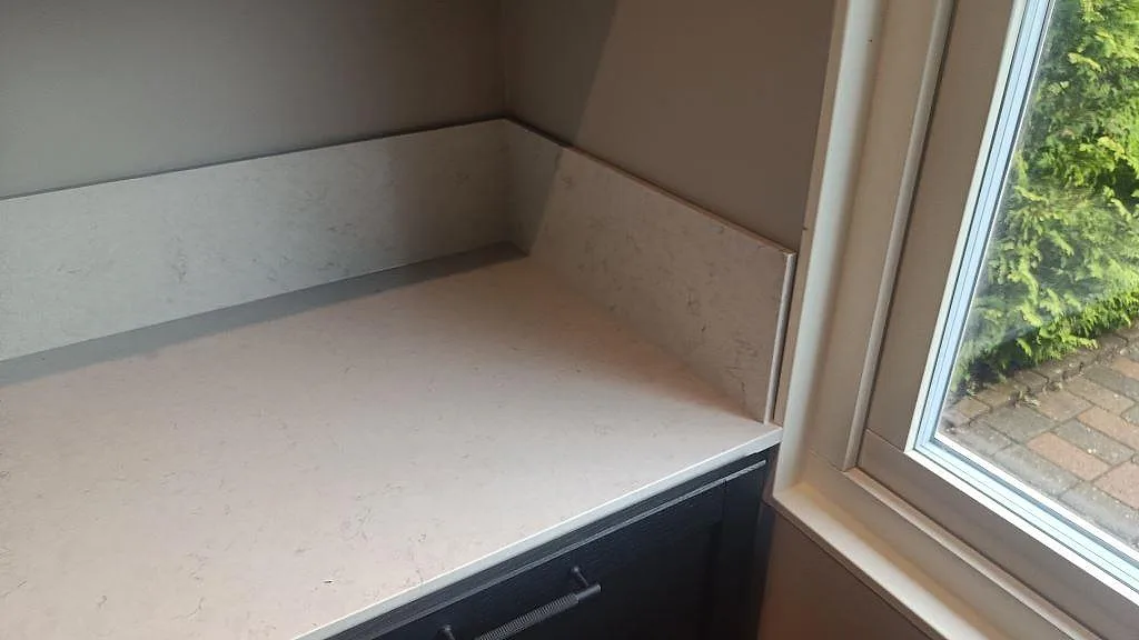 Låg stänkkant och bänkskiva i polerad Silestone Snowy Ibiza vid fönster i kök i Svedala.