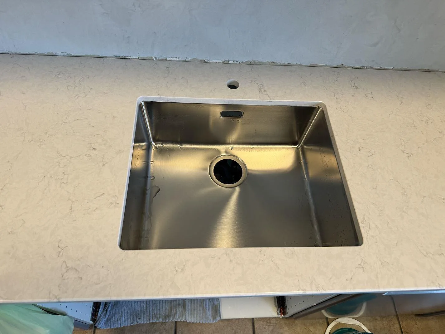 Närbild på rostfri diskho i en polerad Silestone Snowy Ibiza kvartskompositbänkskiva med ljus grå ådring i Svedala.