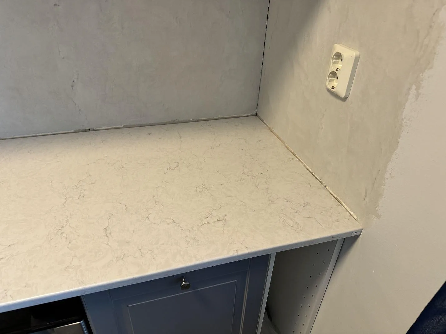 Detalj av polerad Silestone Snowy Ibiza kvartskomposit i hörnläge med grå vägg och köksstommar i Svedala.