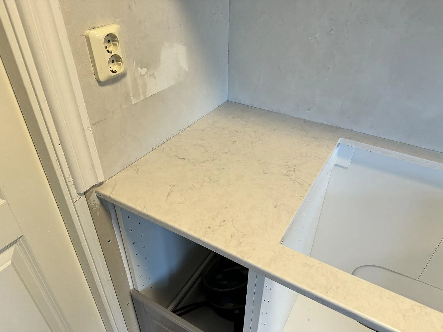 Hörn av köksbänkskiva i polerad Silestone Snowy Ibiza kvartskomposit vid vägguttag och öppna stommar under montering i Svedala.