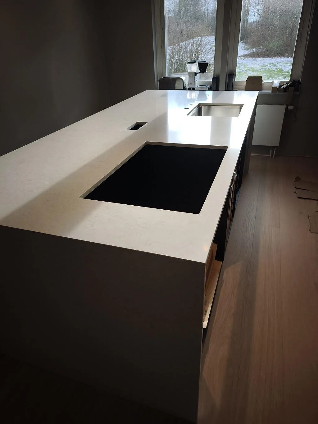Lång polerad Silestone Snowy Ibiza bänkskiva i komposit med svart hällöppning och rostfri diskho vid fönster i Svedala.