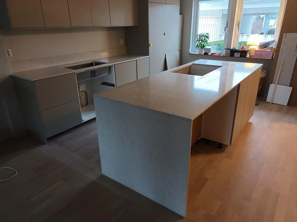 Köksbänkskiva och stor köksö i vit Silestone Snowy Ibiza, polerad komposit med diskret ådring, med förberedda urtag i ett kök under montering i Täby.