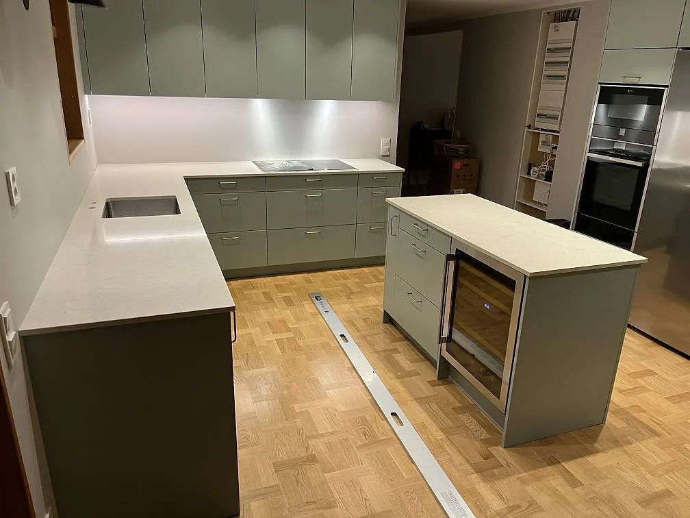 Köksbänkskiva och köksö i vit Silestone Snowy Ibiza, polerad 20 mm kvartskomposit, i ett U-format kök med gröna luckor i Täby.