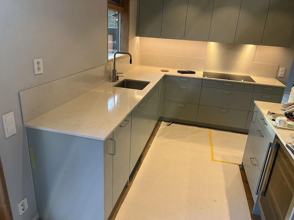 Köksbänkskiva i ljus Silestone Snowy Ibiza, 12 mm polerad komposit, med diskho, häll och uppvikt stänkkant i ett U-format kök i Täby.