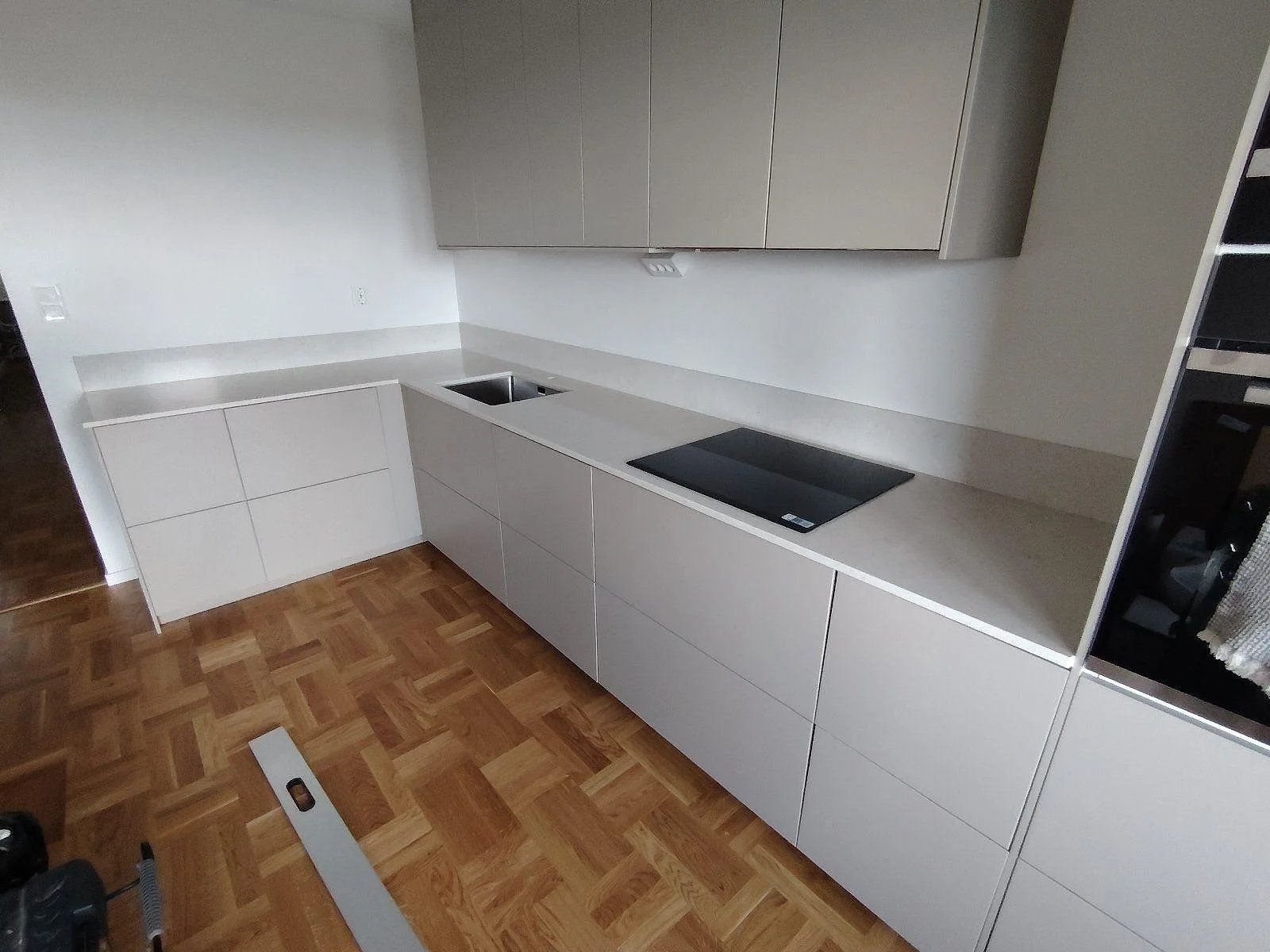 Köksbänkskiva i vit Silestone Snowy Ibiza, polerad komposit, med underlimmad rostfri diskho och svart induktionshäll i ett L-format kök i Täby.