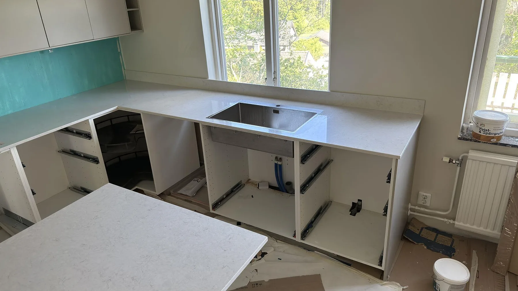 Bänkrad i polerad Silestone Snowy Ibiza med urtagning för diskho och mintgrönt glasstänkskydd i ett kök under montering i Täby.