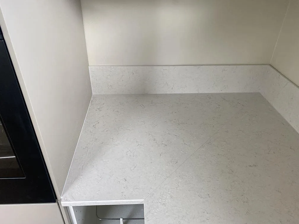 Hörndel av köksbänkskiva i polerad Silestone Snowy Ibiza kvartskomposit med 12 mm stänkskydd i köket i Tingsryd.