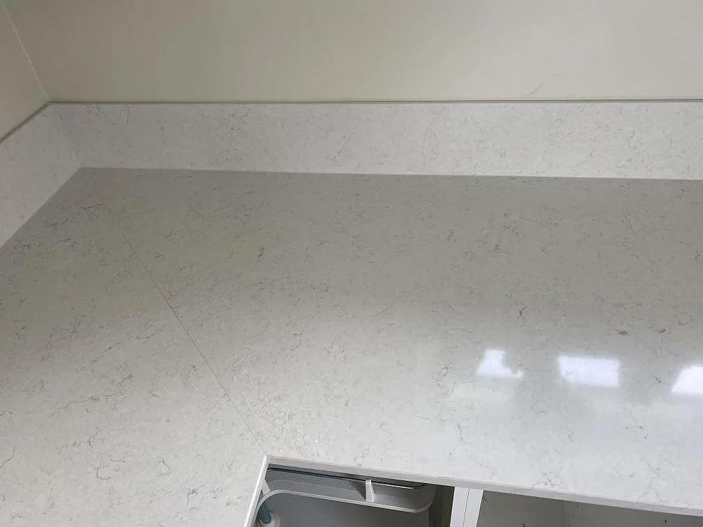 Närbild på polerad Silestone Snowy Ibiza kvartskomposit med underlimmad rostfri Stala-diskho och stänkskydd i köket i Tingsryd.