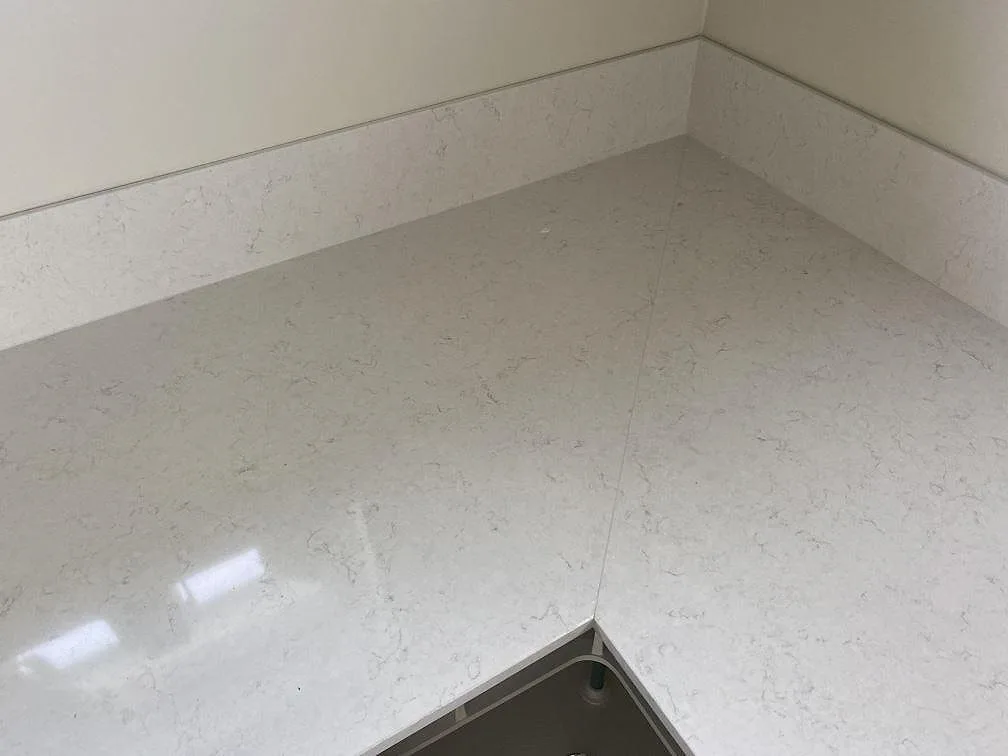 Detalj av polerad Silestone Snowy Ibiza kvartskomposit runt diskhoöppning och stänkskydd i köket i Tingsryd.
