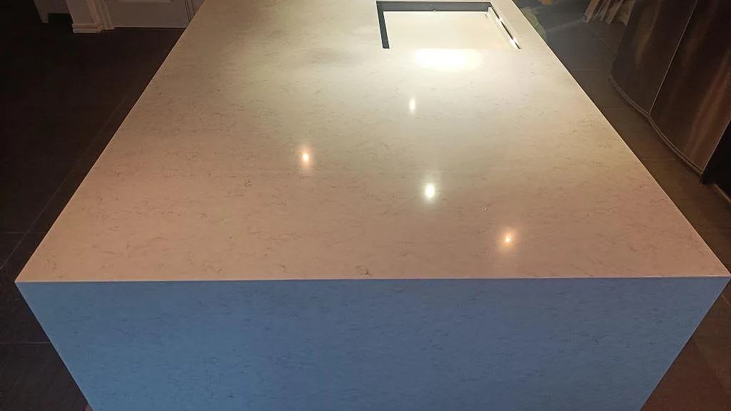 Polerad köksö i Silestone Snowy Ibiza, kvartskomposit, med ljus ådring och rektangulärt urtag i Tomelilla.