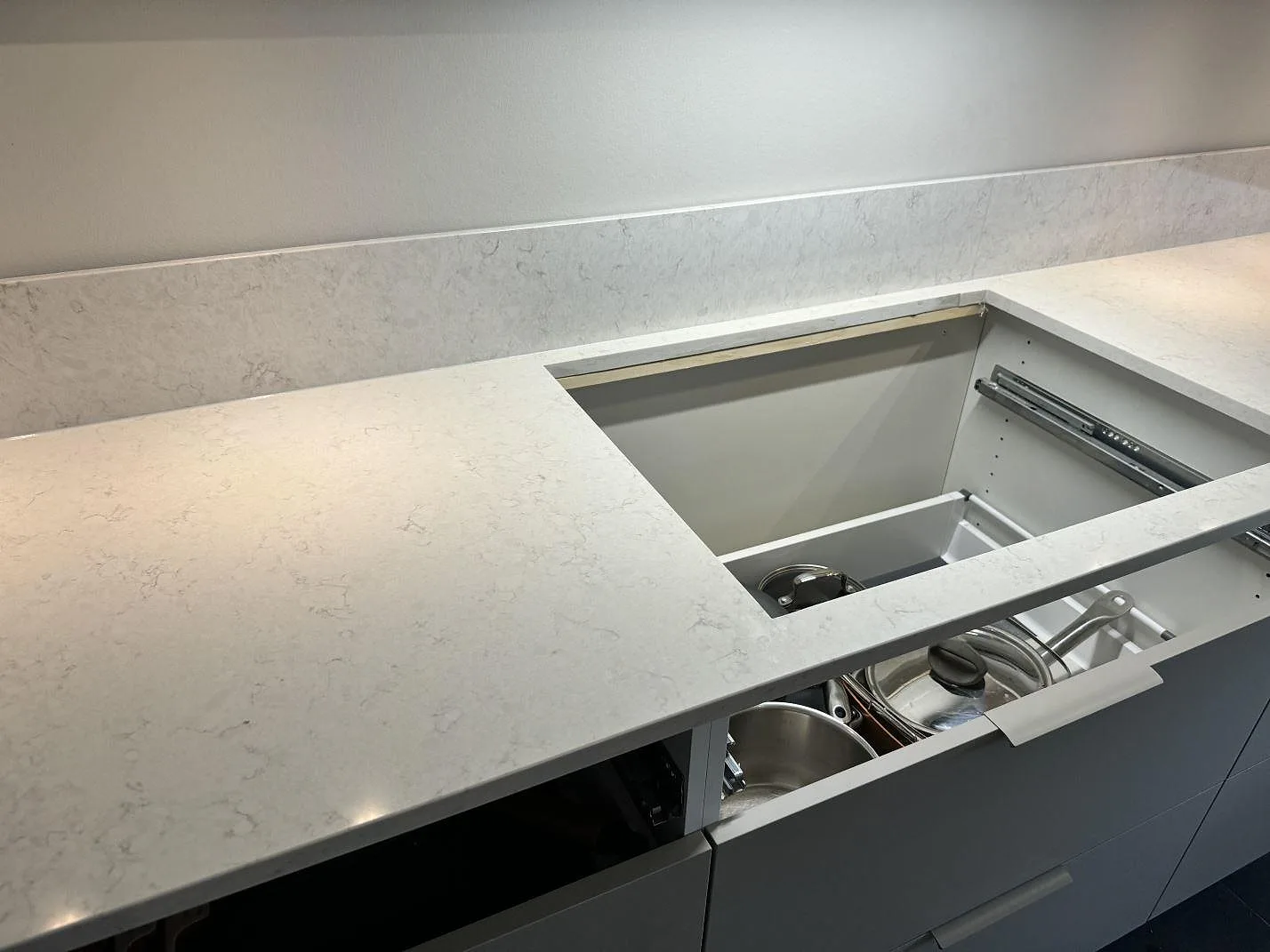 L-formad köksbänkskiva i polerad Silestone Snowy Ibiza med stänkskydd och utdragen låda under monteringen i Torslanda.