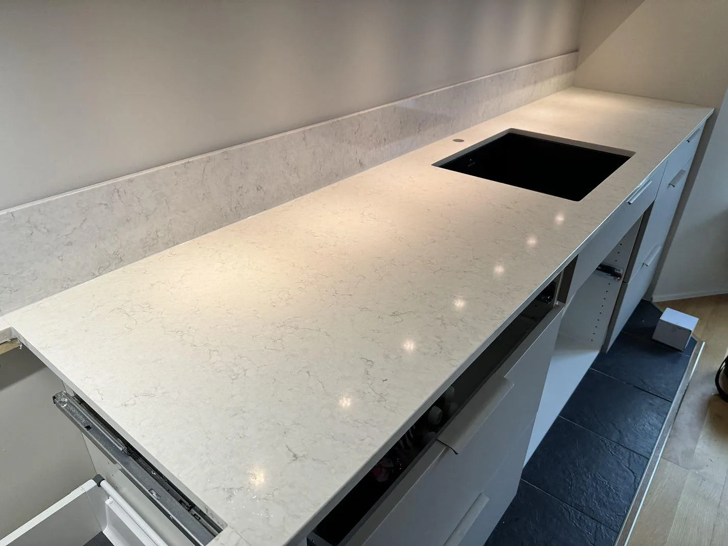 Köksbänkskiva i polerad Silestone Snowy Ibiza, 20 mm kvartskomposit, med svart diskho ovanpå stenen och stänkskydd i ett kök i Torslanda.