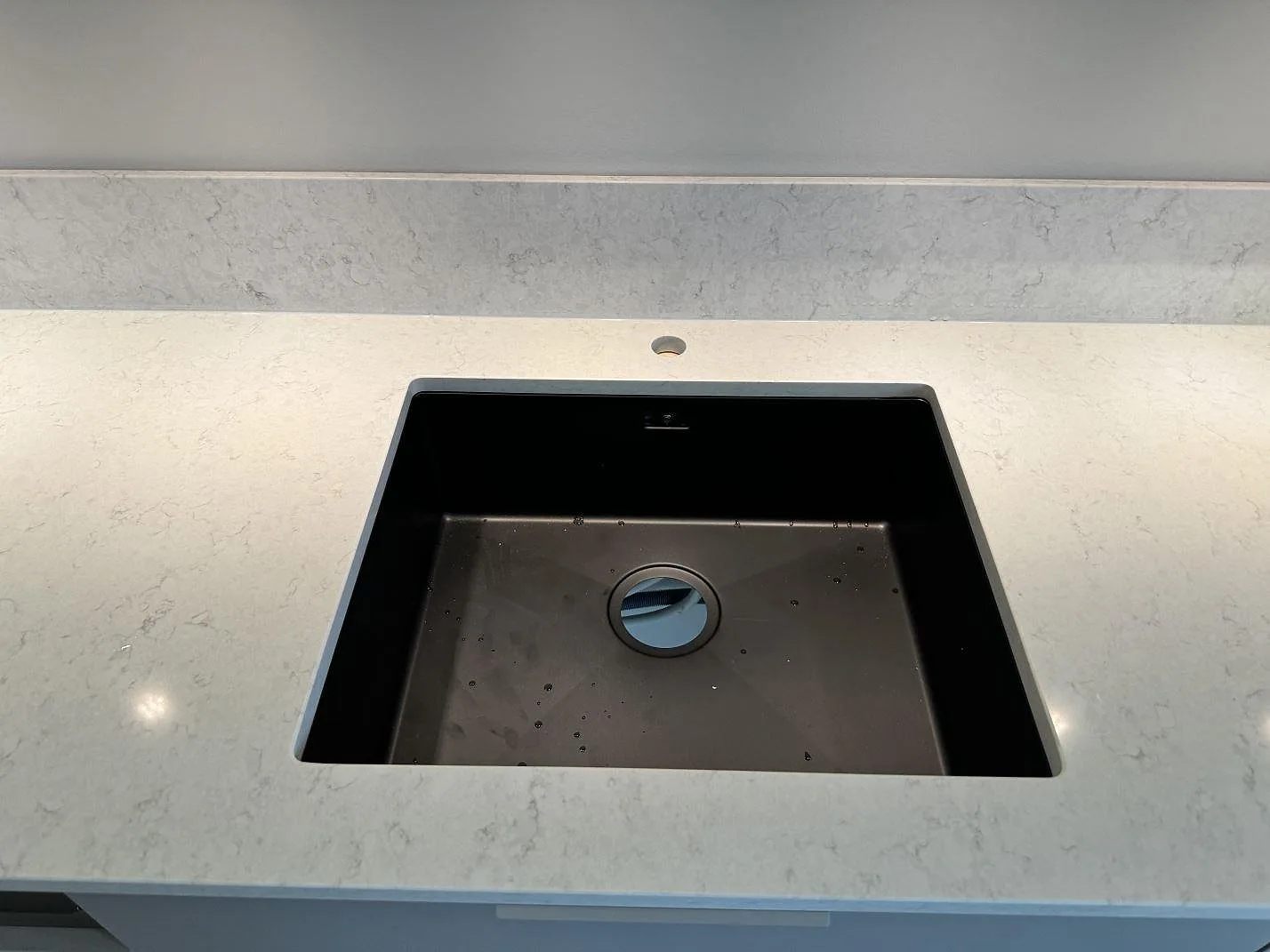 Närbild på svart diskho ovanpå köksbänkskiva i polerad Silestone Snowy Ibiza med blandarhål och stänkskydd i Torslanda.