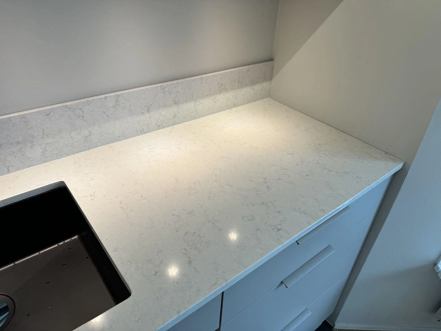 Höger del av L-formad köksbänkskiva i polerad Silestone Snowy Ibiza med svart diskho och ljus ådring i Torslanda.