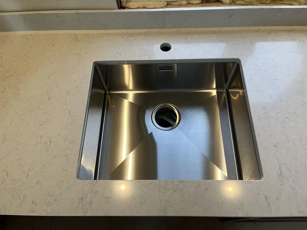 Närbild på rostfri underlimmad diskho i en polerad Silestone Snowy Ibiza bänkskiva i kök i Tranås.