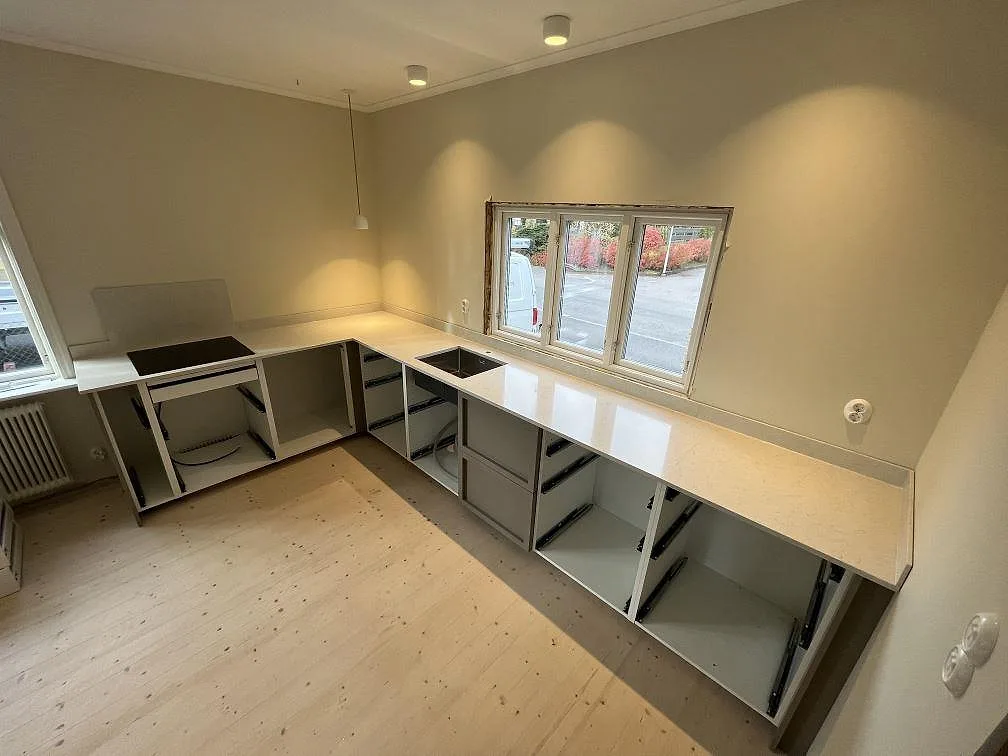 U-formad köksbänkskiva i Silestone Snowy Ibiza, polerad komposit, med svart induktionshäll och rostfri diskho i ett kök i Tranås.