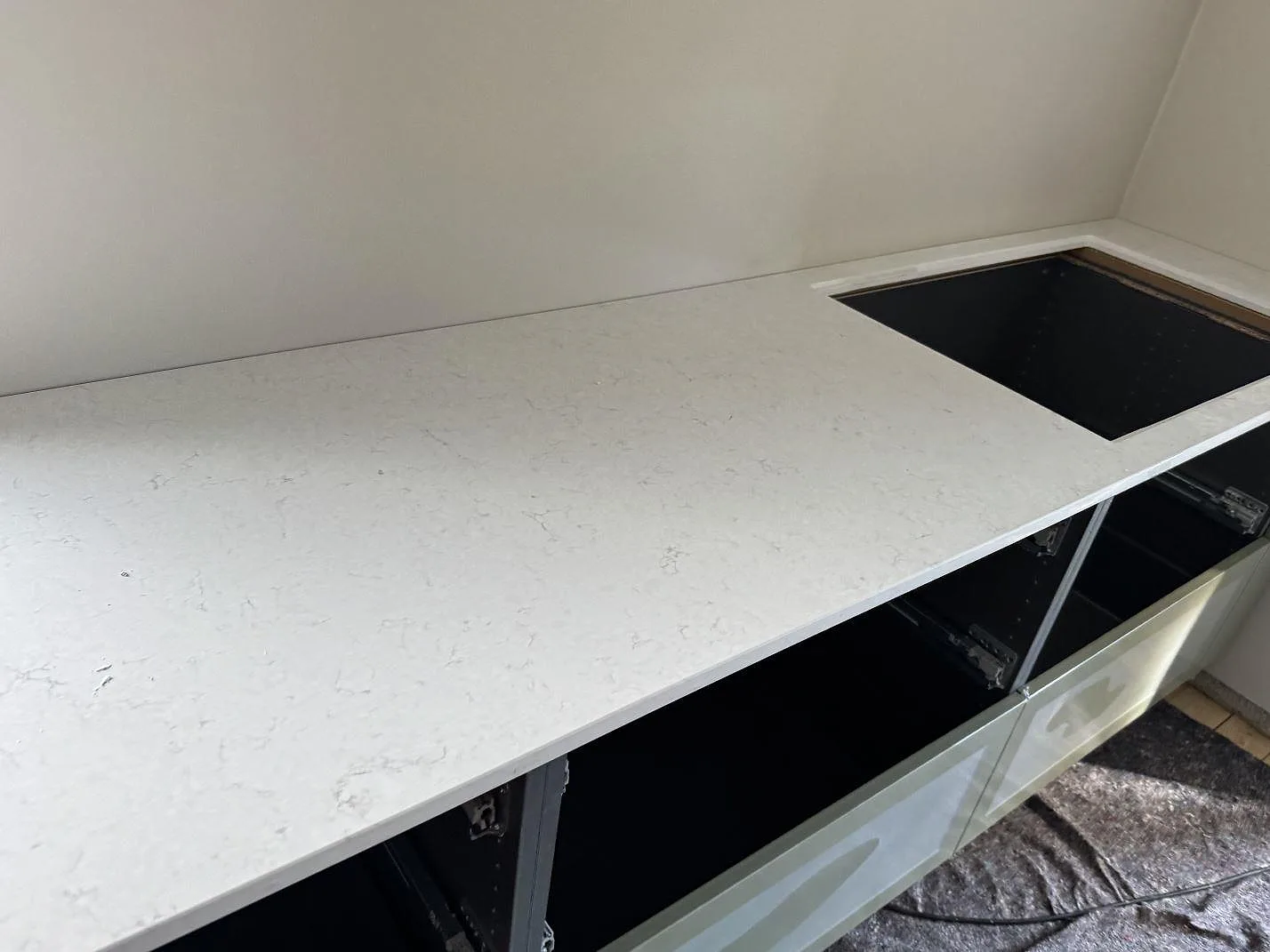 Polerad kvartskomposit Silestone Snowy Ibiza som köksbänk med utskuren hällöppning över öppna skåpstommar i Trelleborg.