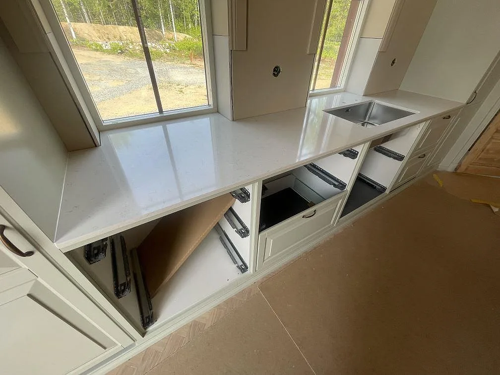 Lång fönsterrad med polerad Silestone Snowy Ibiza bänkskiva och rostfri diskho monterad över vit köksinredning i Trosa.