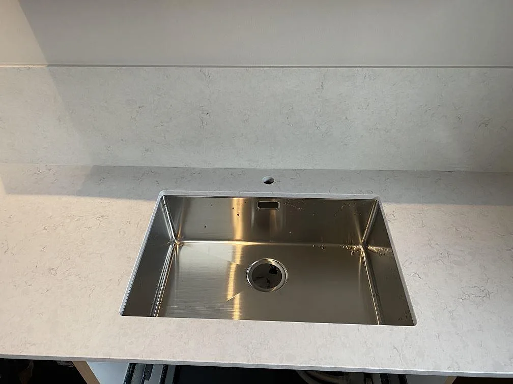 Detalj av polerad Silestone Snowy Ibiza runt en rostfri diskho och matchande stänkskydd i köket i Tygelsjö.
