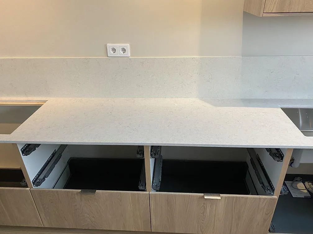 Rak köksbänk i polerad Silestone Snowy Ibiza med öppna köksstommar, stänkskydd och utskärningar för häll och diskho i Tygelsjö.