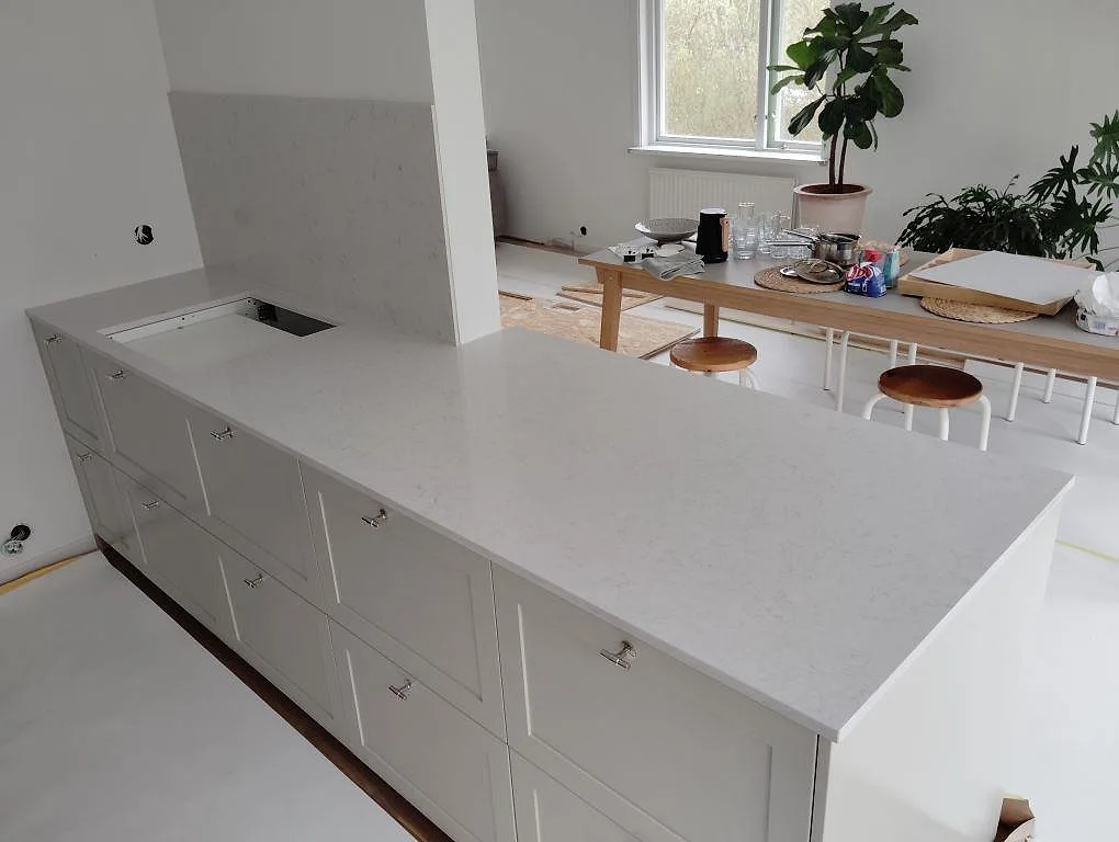 Köksbänkskiva i ljus Silestone Snowy Ibiza, polerad, med hällurtag och stänkskydd i ett öppet kök i Tyresö.