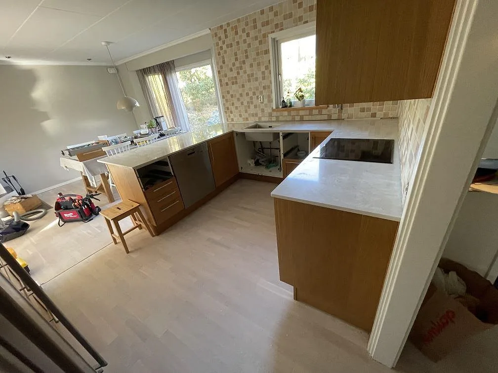 Polerad köksbänkskiva i Silestone Snowy Ibiza längs träskåp och kaklad vägg, med häll och montering pågående i Tyresö.