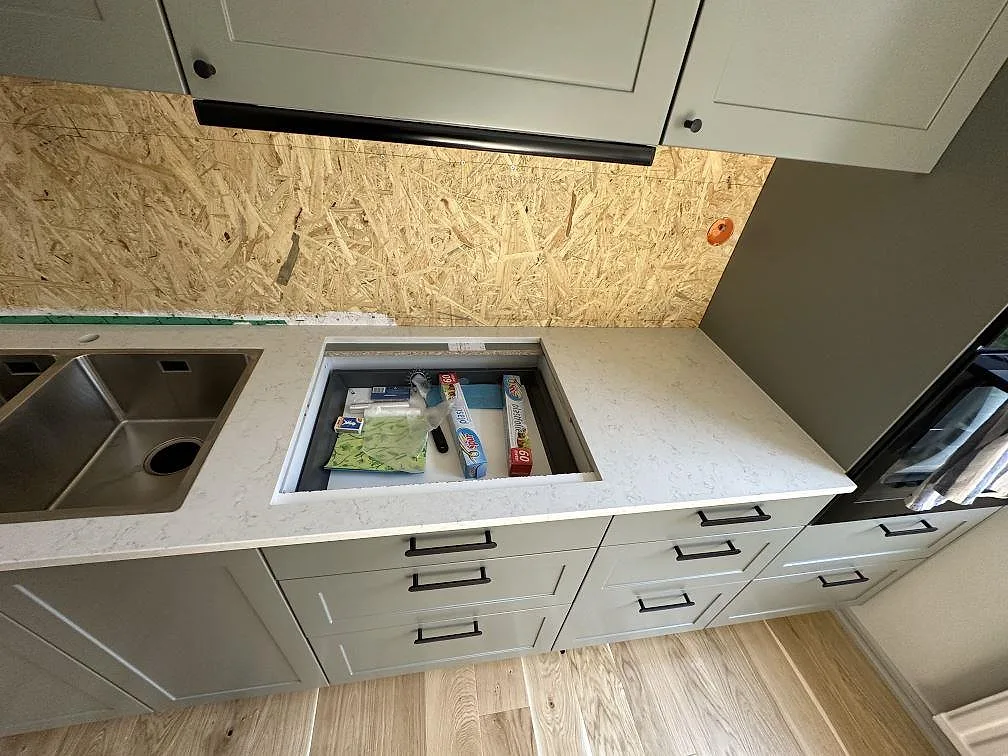 L-formad köksbänkskiva i Silestone Snowy Ibiza, polerad komposit, med dubbelho och hällöppning under montering i Uddevalla.
