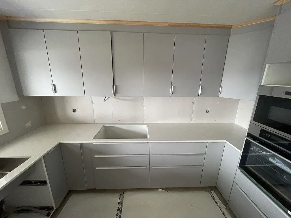 Bänkskiva i polerad vit Silestone Snowy Ibiza längs köksvägg med urtag och inbyggd ugnsstack i ett kök i Ulricehamn.