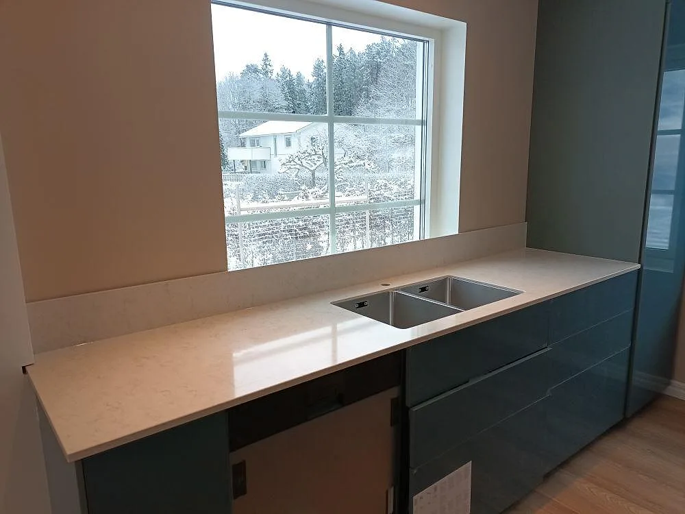 Polerad Silestone Snowy Ibiza som köksbänkskiva med låg stänkkant och synlig diskzon i ett kök i Upplands Väsby.
