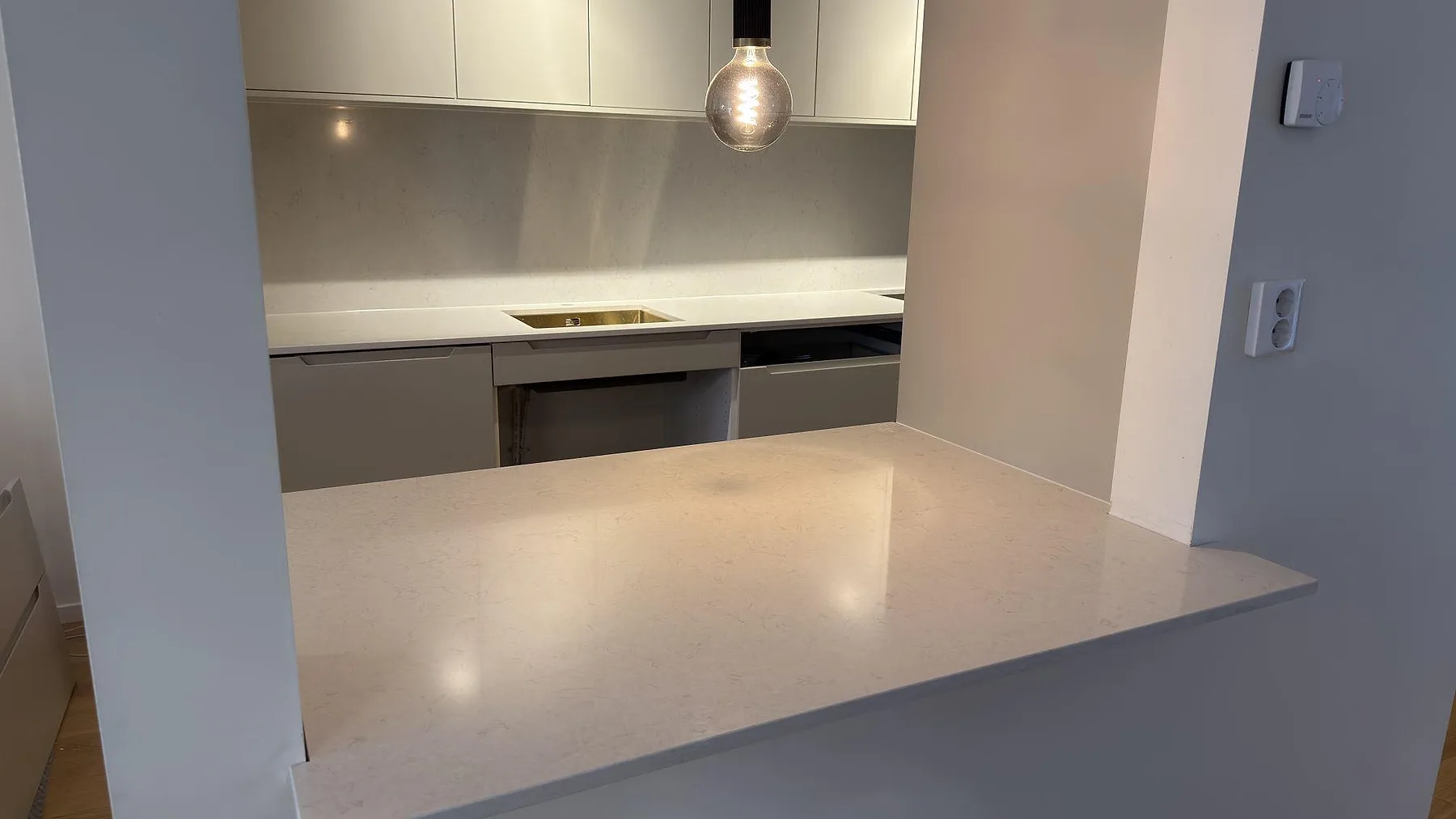 Polerad Silestone Snowy Ibiza som serveringsyta och köksbänkskiva med stänkskydd i en öppen köksmontering i Upplands Väsby.