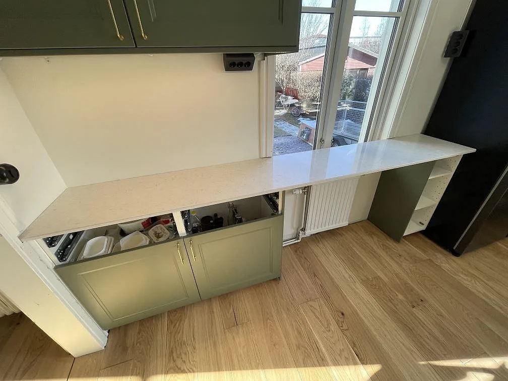Vit Silestone Snowy Ibiza bänkskiva med polerad yta längs en köksdel med sågröna luckor och fönster i ett kök i Uppsala.