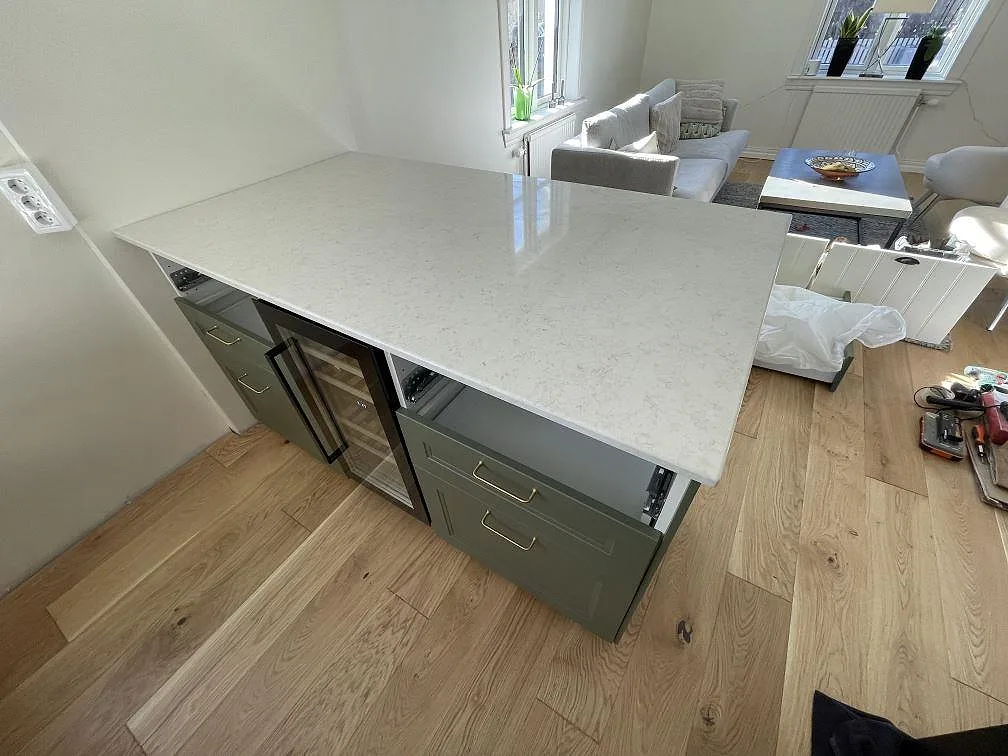 Köksö i vit Silestone Snowy Ibiza med polerad yta och inbyggd vinkyl, öppen mot vardagsrummet, i ett kök i Uppsala.