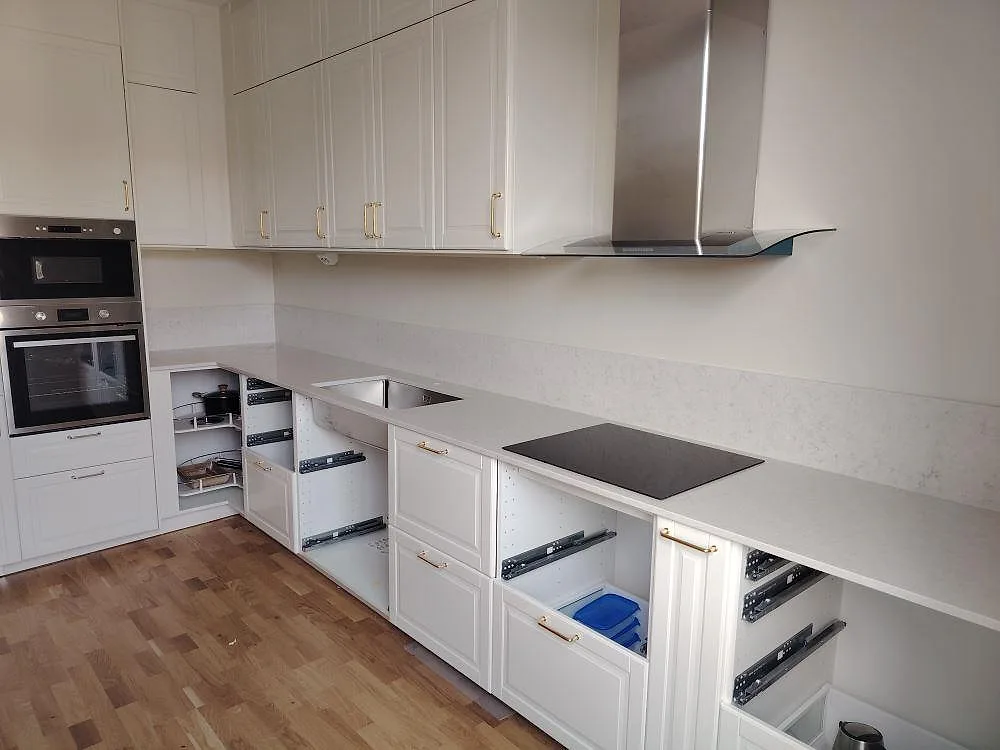 Köksbänkskiva och stänkskydd i vit Silestone Snowy Ibiza, polerad kvartskomposit, med induktionshäll i ett kök i Västerås under montering.